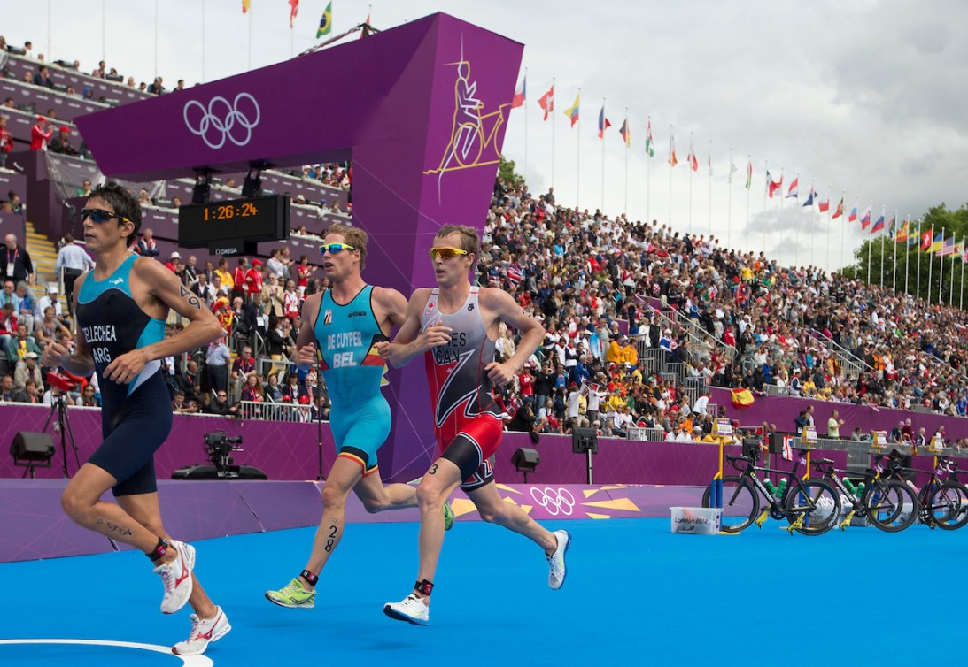 Three triathletes run on a blue carpet