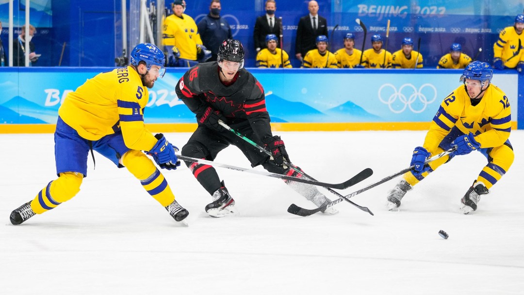 Adam Tambellini between two Swedish players tries to get to the puck with his stick